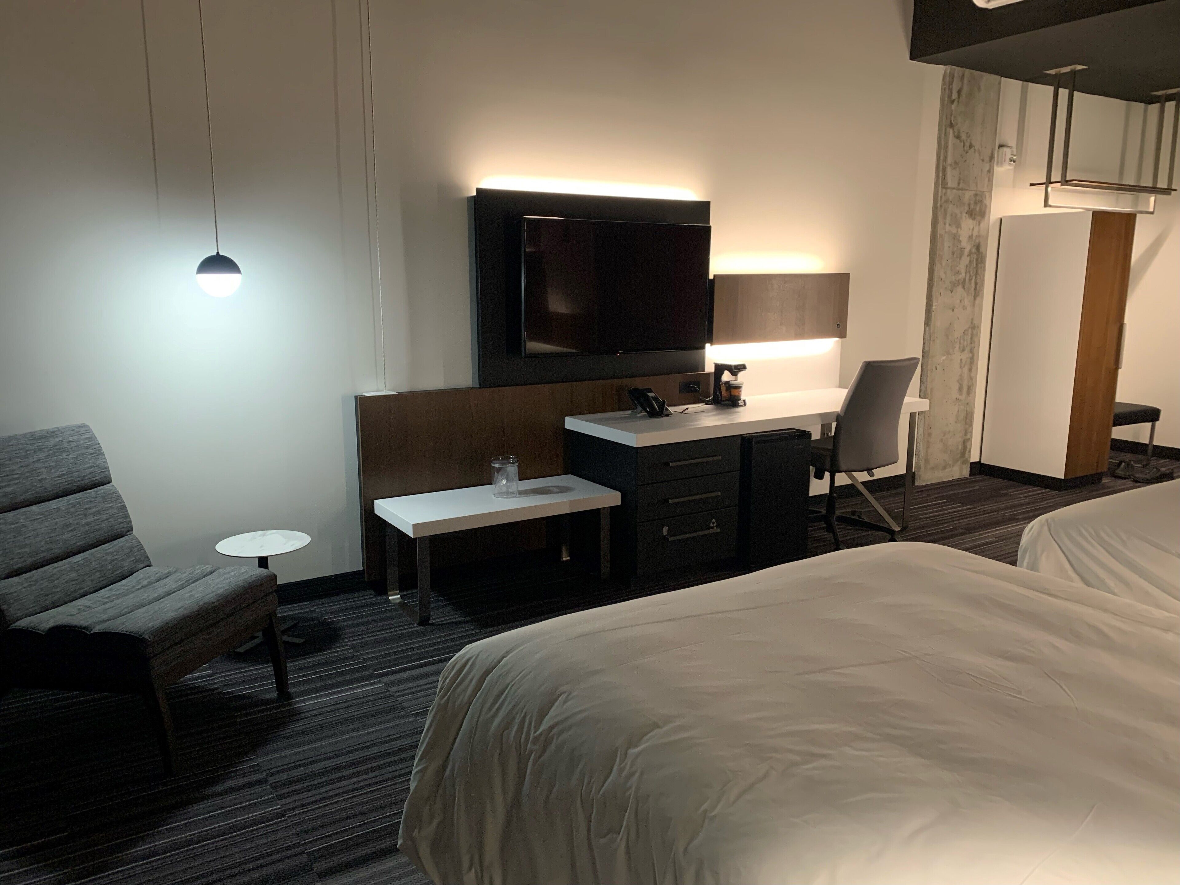 A hotel room with a bed, a desk with a chair, a television, and a small table.