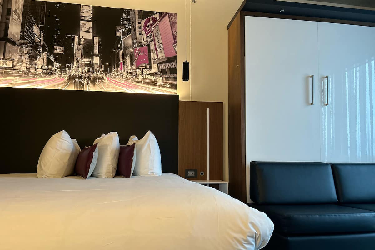A hotel room with a large bed, a black sofa, a wardrobe, and a cityscape mural on the wall.
