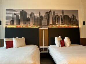 A hotel room with two beds, each with white bedding and red pillows, and a large cityscape mural on the wall. - Grand Hôtel TiMES Blainville - Mirabel (Blainville)