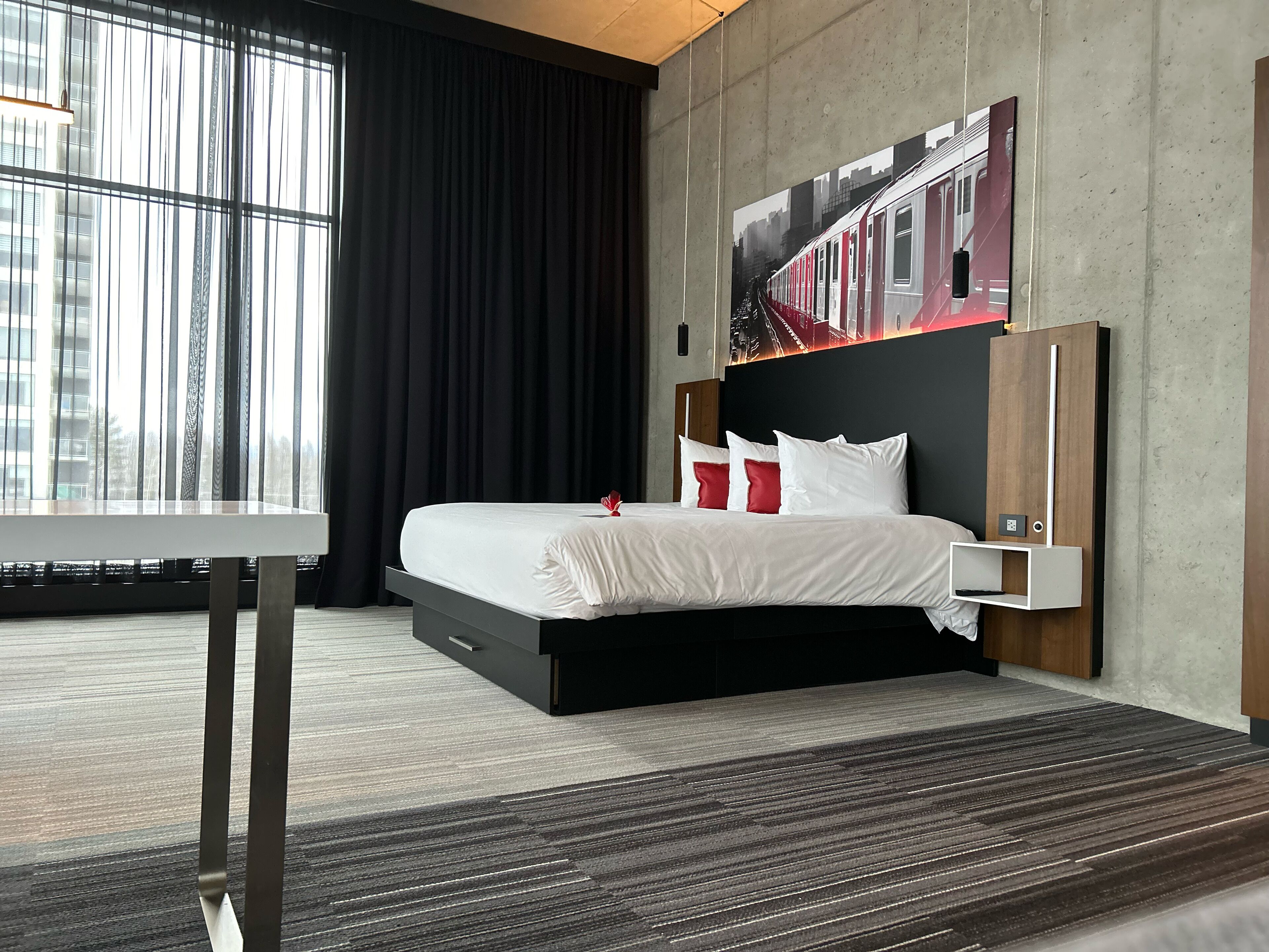 Ein modernes Hotelzimmer mit einem großen Bett, einem Schreibtisch und einem Stadtbild an der Wand.