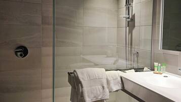 Un baño moderno con ducha envuelta en cristal, un lavabo blanco y un espejo grande.