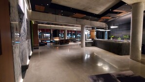 Um hall amplo com piso de concreto polido, balcão de recepção e áreas de estar.