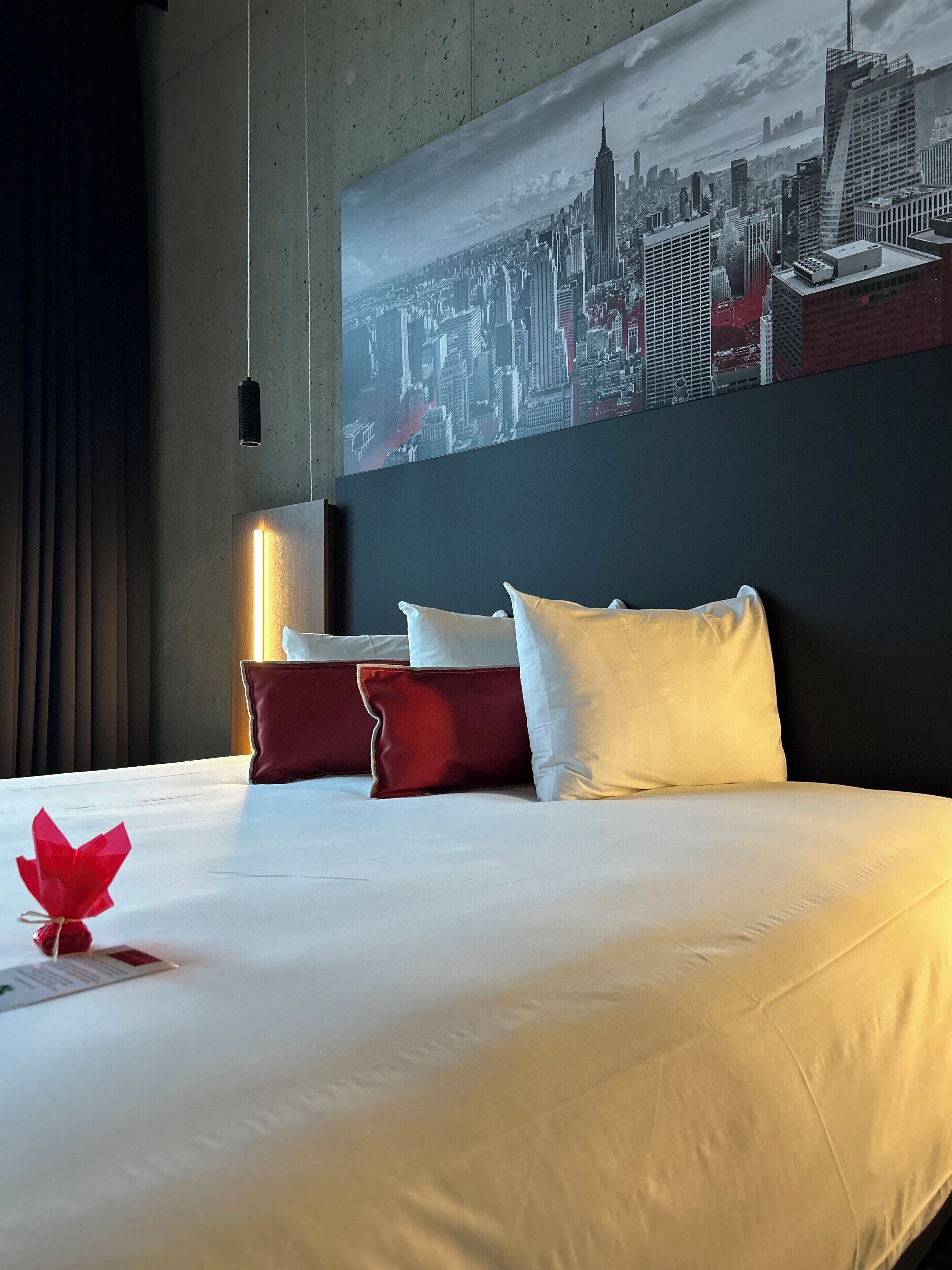 Hotelkamer met een groot bed, een stadsgezichtschilderij aan de muur en een rode decoratie op het bed.