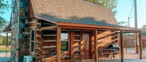 A rustic log cabin with a stone chimney, a covered porch, and a grill outside.