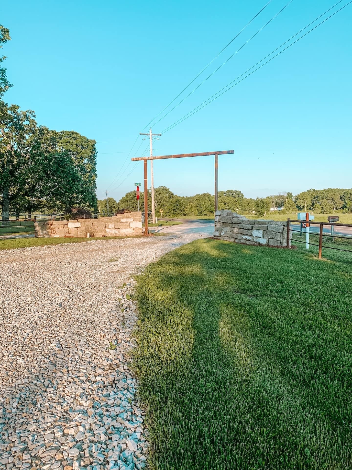 A rural intersection with a stop sign, stone wall, and gravel path.