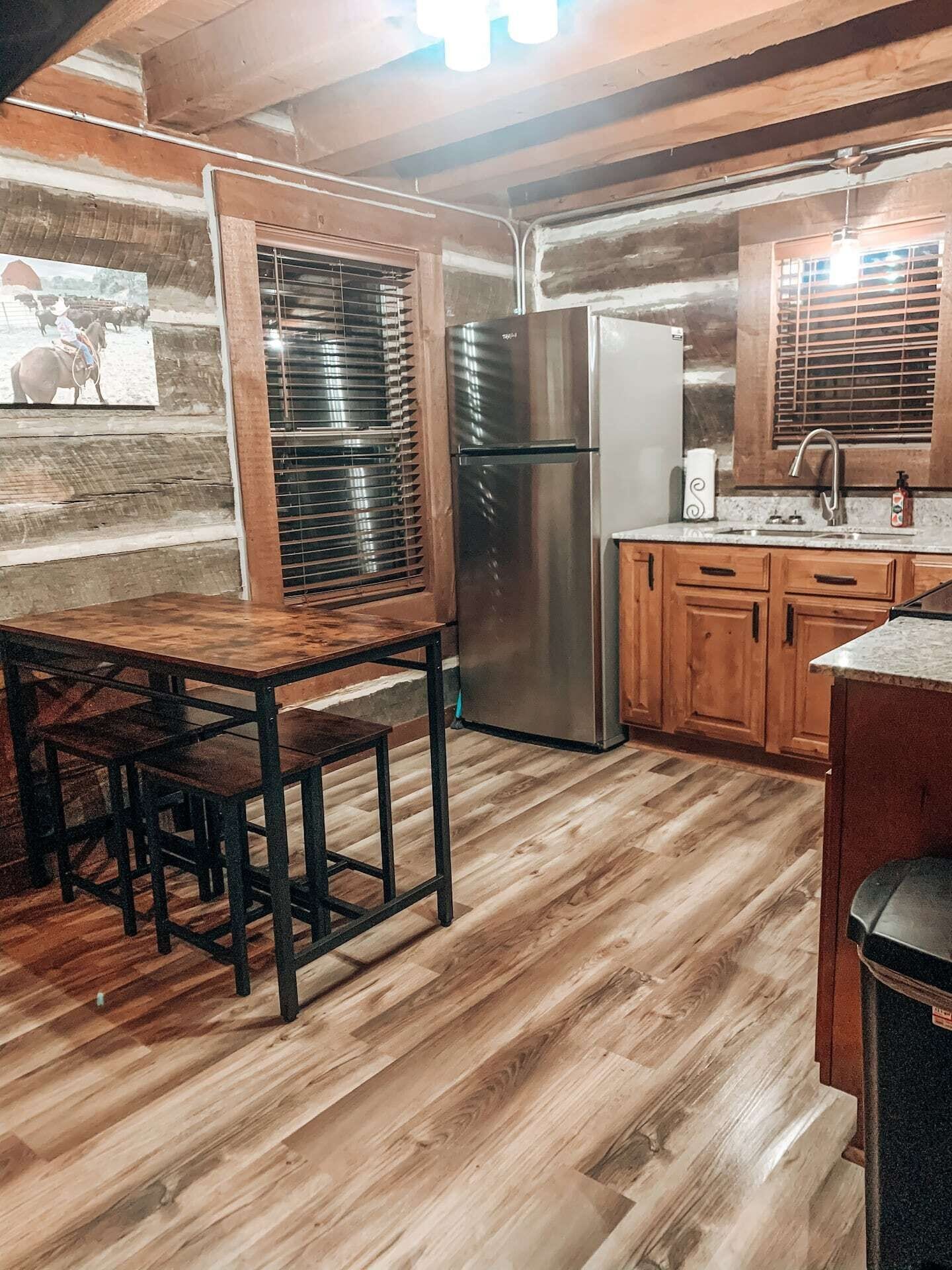 Une cuisine rustique avec des meubles de rangement en bois, un réfrigérateur en acier inoxydable et une table à manger en bois, accompagnée de chaises.