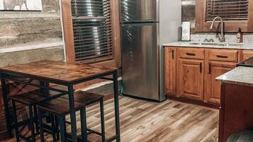 Une cuisine rustique avec des meubles de rangement en bois, un réfrigérateur en acier inoxydable et une table à manger en bois, accompagnée de chaises.