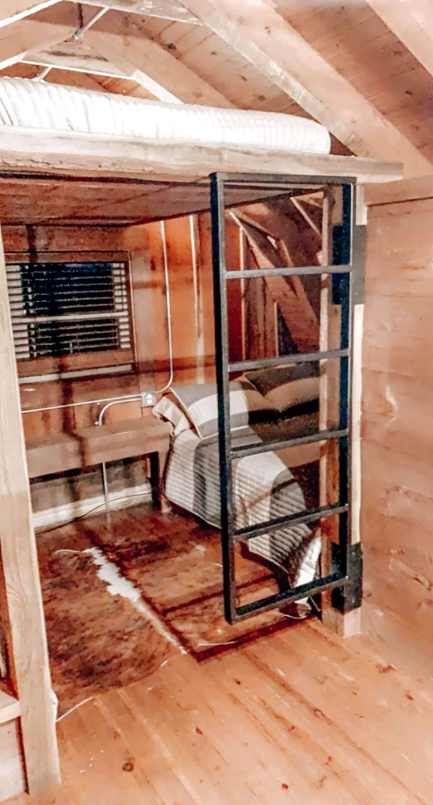 Une petite chambre mansardée au charme rustique, avec un lit en mezzanine, une fenêtre équipée de stores et un plancher en bois.