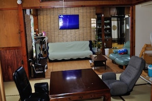 A living room with a sofa, a dining table, and a TV mounted on the wall.