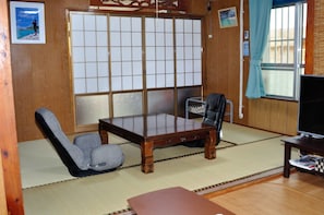 A traditional Japanese room with tatami flooring, a low table, a chair, a TV, and a sliding door with a grid pattern. - Yukuiru (Miyakojima)