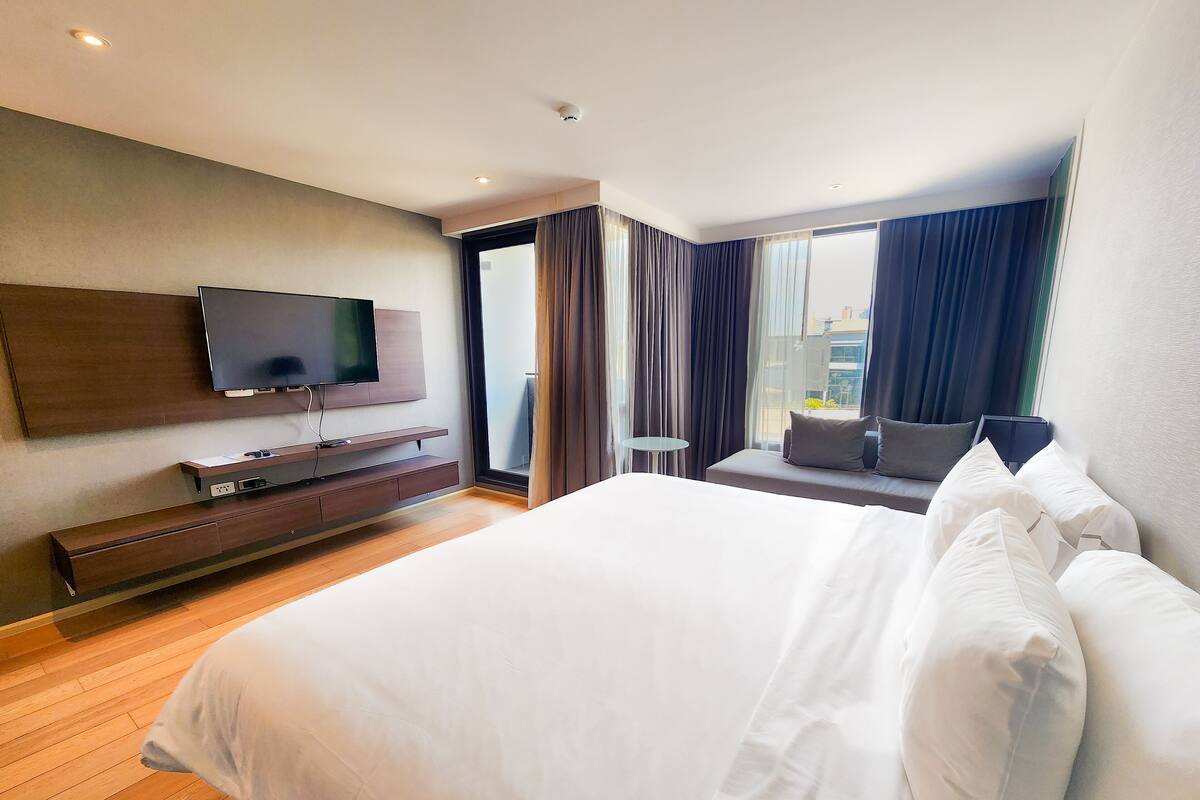 Une chambre d’hôtel moderne dotée d’un grand lit, d’un téléviseur à écran plat fixé au mur, d’une petite table d’appoint et offrant une vue sur la ville par la fenêtre.