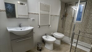 Ein Badezimmer mit Waschbecken, Bidet, Toilette, Dusche und einem beleuchteten Spiegel.