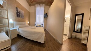 Ein Schlafzimmer mit einem großen Bett, Nachttischen, einem an der Wand befestigten Fernseher und einem Fenster mit Vorhängen.