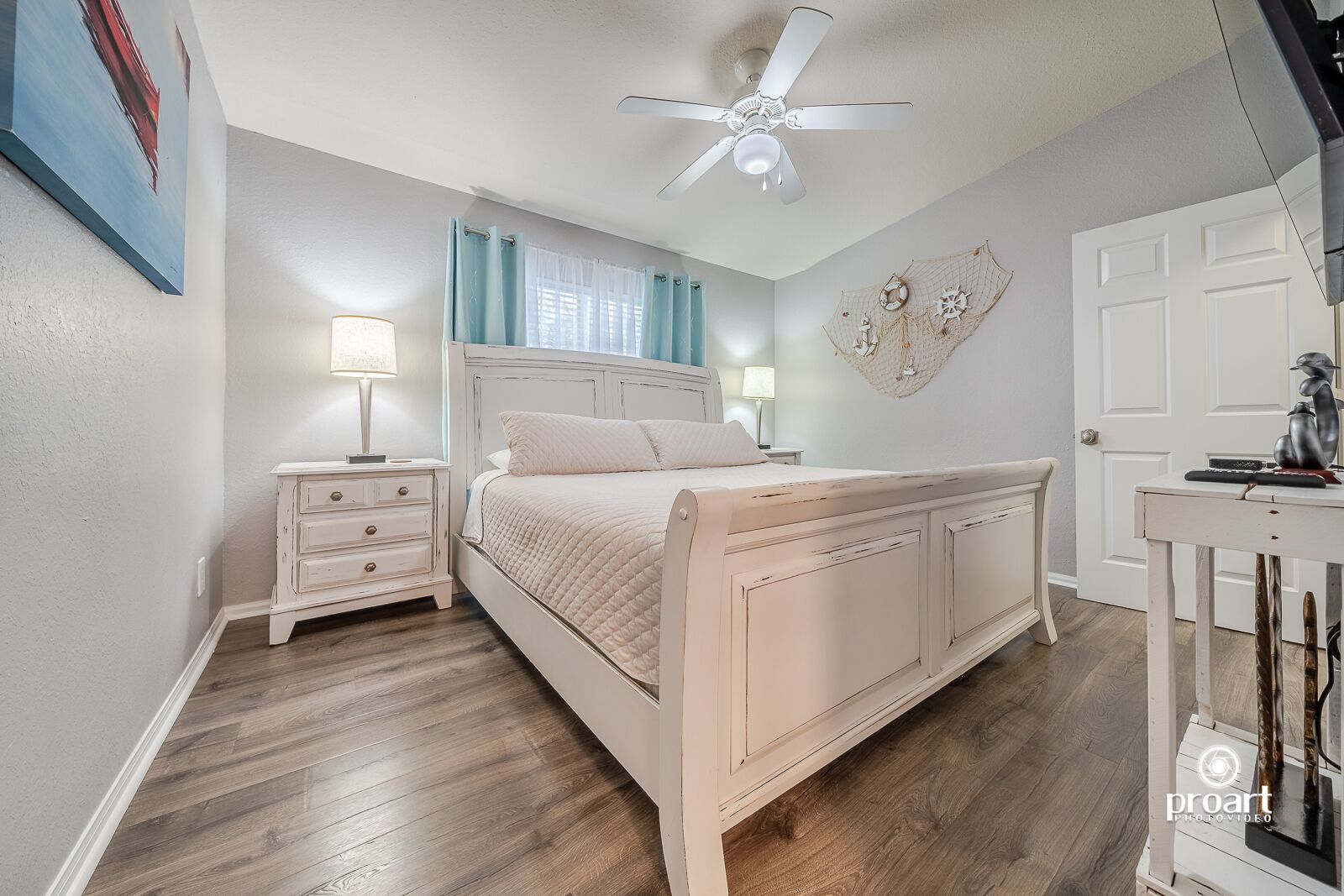 Quarto com cama, mesas de cabeceira, ventilador de teto e uma porta.