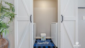 Een wasserette met een zwart-wit geruit vloermatje met de tekst 'Laundry Room', een witte wasmachine en een witte droger.