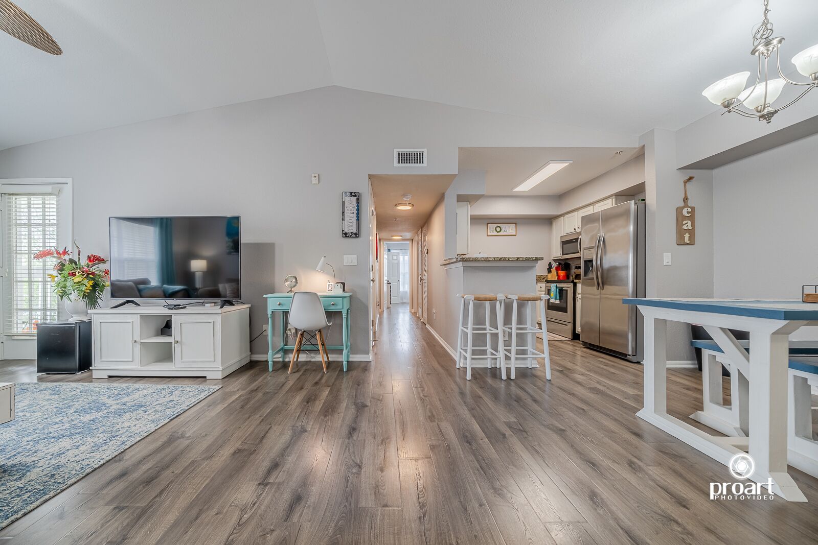 A modern kitchen with a built-in oven, a stainless steel refrigerator, and a dining area with a blue table and white bar stools.