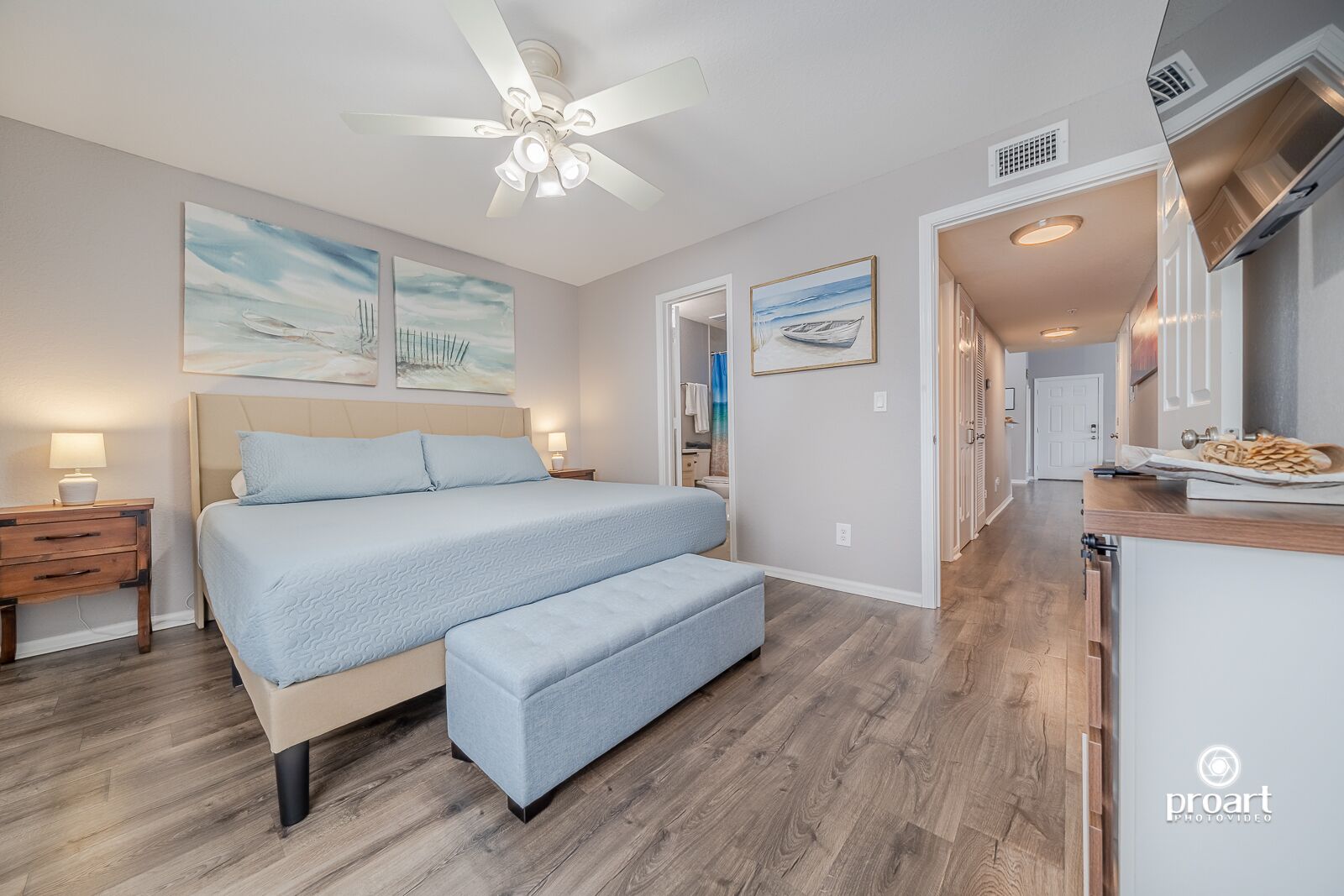 A bedroom with a bed, bedside tables, a ceiling fan, and artwork on the walls.