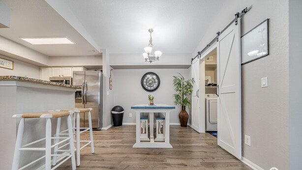 Een moderne keuken met een centraal eiland, barstoelen, een klok en een hangende lamp.