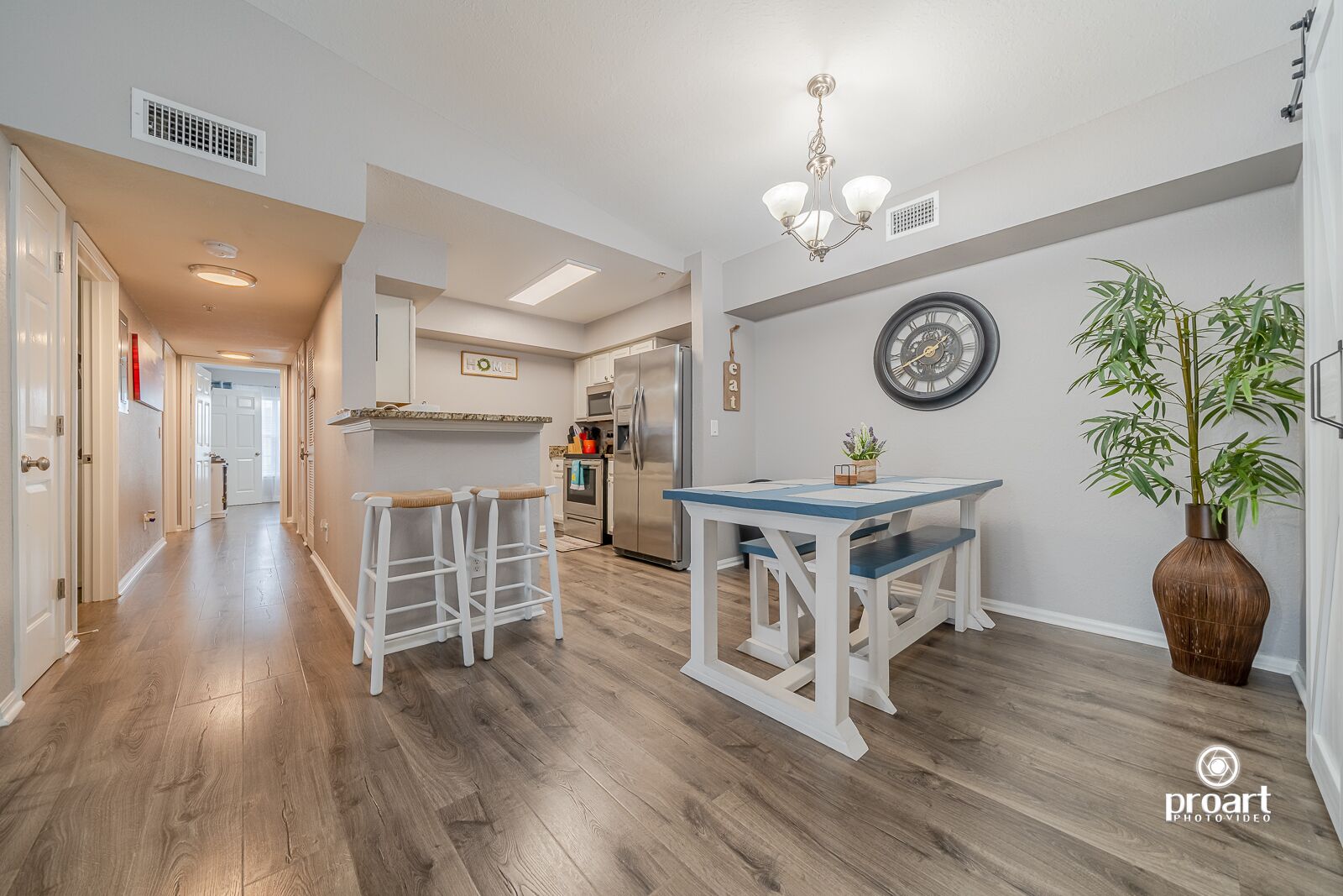 A modern kitchen with a dining area, wooden flooring, and a large clock on the wall.