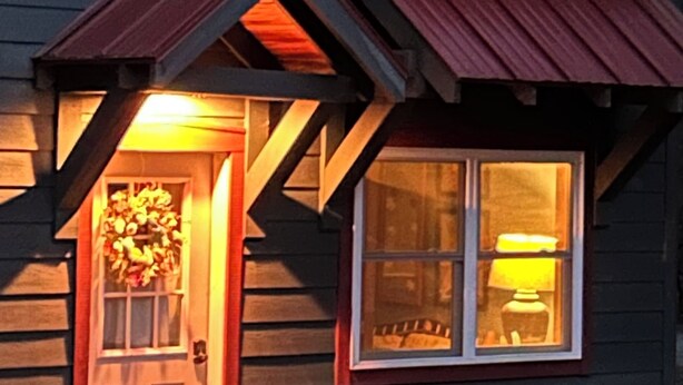 Et træhus med en fordør og et vindue med en lampe indeni.