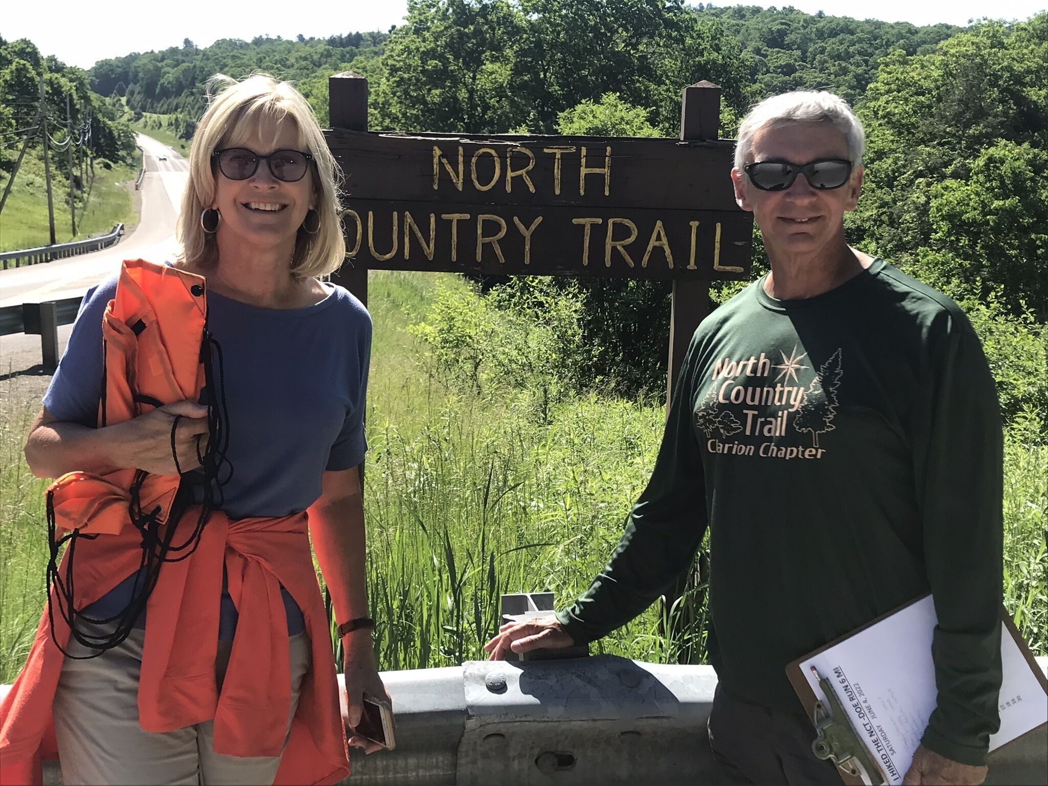 Deux personnes se tiennent devant un panneau indiquant le « North Country Trail », avec une forêt en arrière-plan.