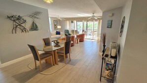 A spacious living room with a glass dining table, comfortable seating, a ceiling fan, and a view to the outside. - Pickleball, beach, pool, tennis, nextdoor to Publix, Junkanoo's and Fresh Catch. (Fort Myers Beach)