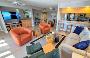 Una sala de estar moderna con sofás de cuero, una mesa de centro de vidrio y un televisor que muestra una escena de playa.