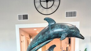 A lobby with a large clock, a dolphin sculpture, and a tiled floor. - Pickleball, beach, pool, tennis, nextdoor to Publix, Junkanoo's and Fresh Catch. (Fort Myers Beach)