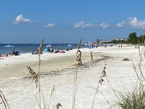 Una playa con arena, vegetación escasa y sombrillas.