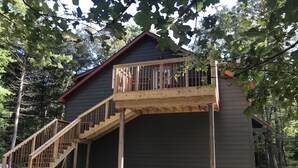 Une terrasse en bois avec un escalier menant à une zone abritée, le tout entouré d’arbres.