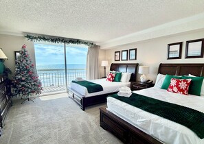 Een hotelkamer met twee bedden, een kerstboom, een balkon met uitzicht op het strand en een groot raam.