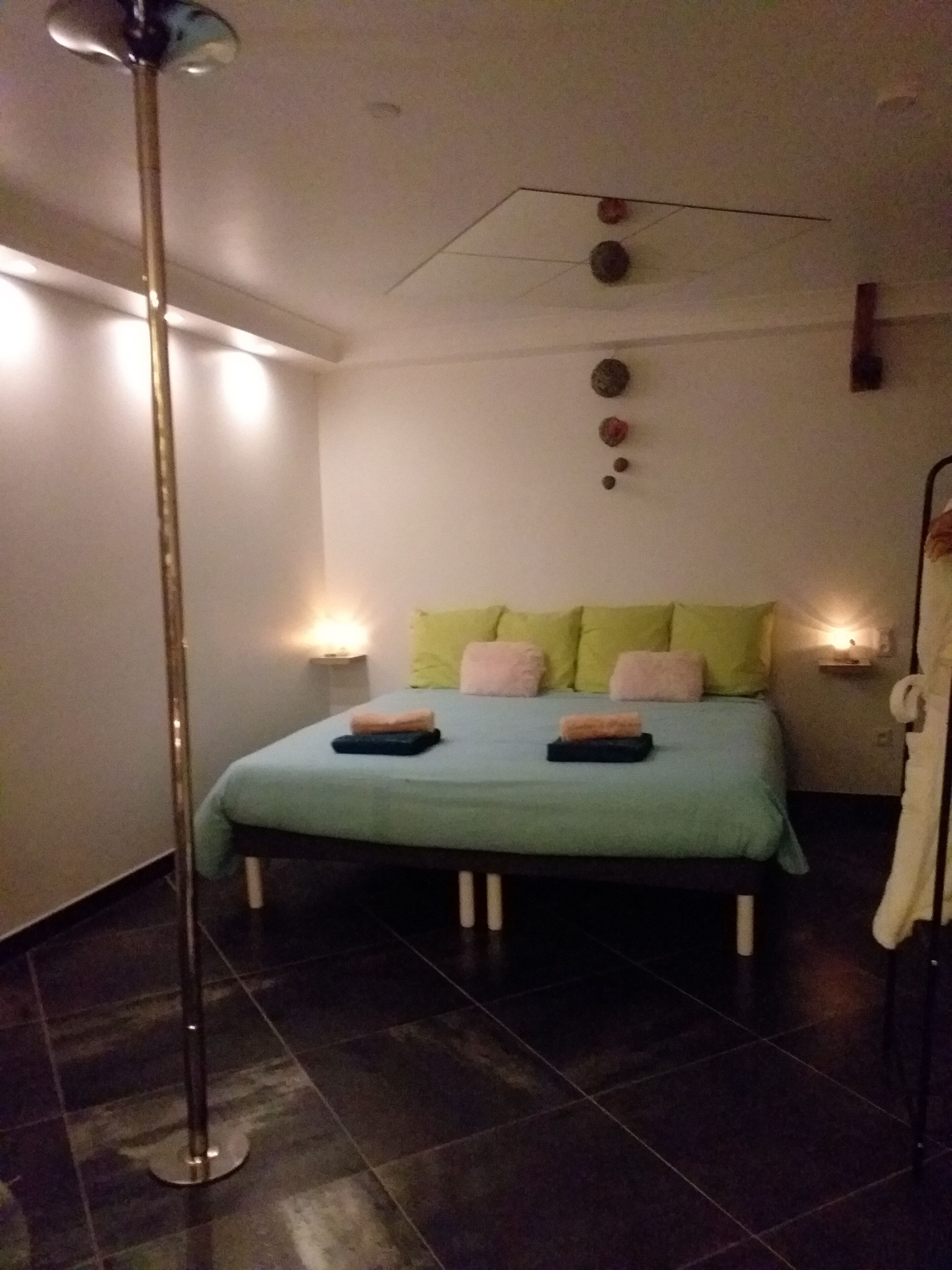 A bedroom with a bed, a floor lamp, and a wall-mounted light fixture.