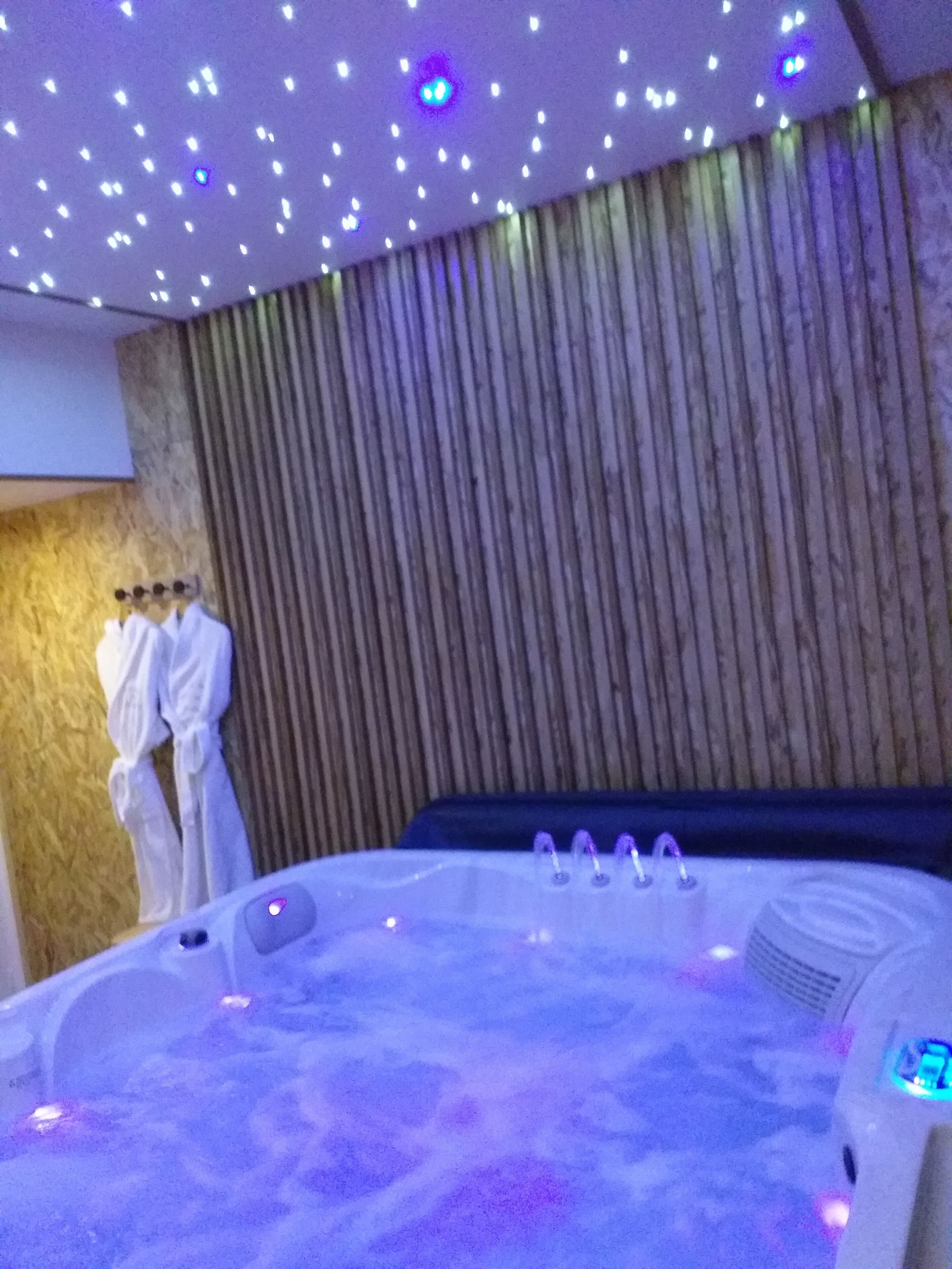 Habitación de spa con hidromasaje, pared de paneles de madera y un perchero para batas.