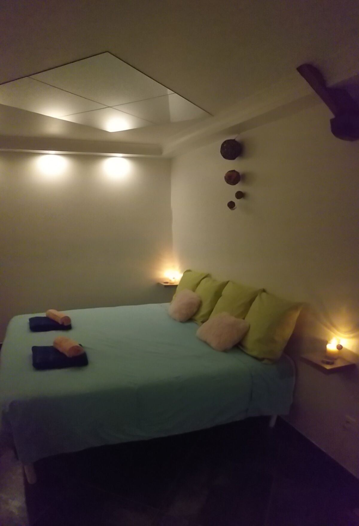 Ett litet, svagt upplyst rum med en enkel säng, ett litet bord och en väggmonterad lampa.