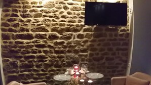Un rincón comedor acogedor con una pared de piedra, un televisor de pantalla plana sobre una mesa adornada con velas, y dos sillones.