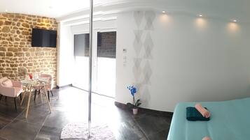 A room with a bed, a stone wall, a TV, and a dining area with a table and chairs.