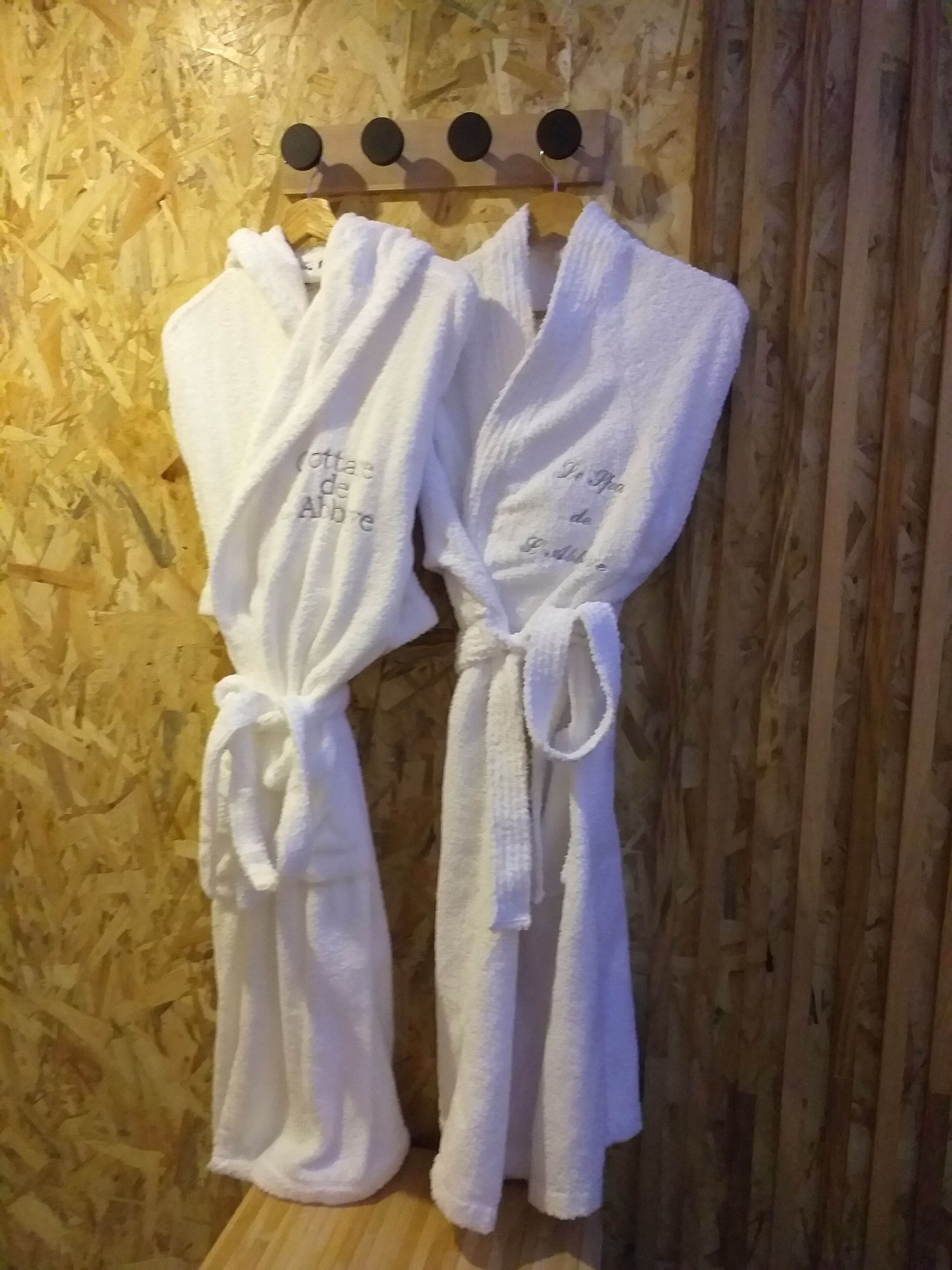 Deux peignoirs blancs sont suspendus à un porte-serviettes en bois, adossé à un mur en bois.