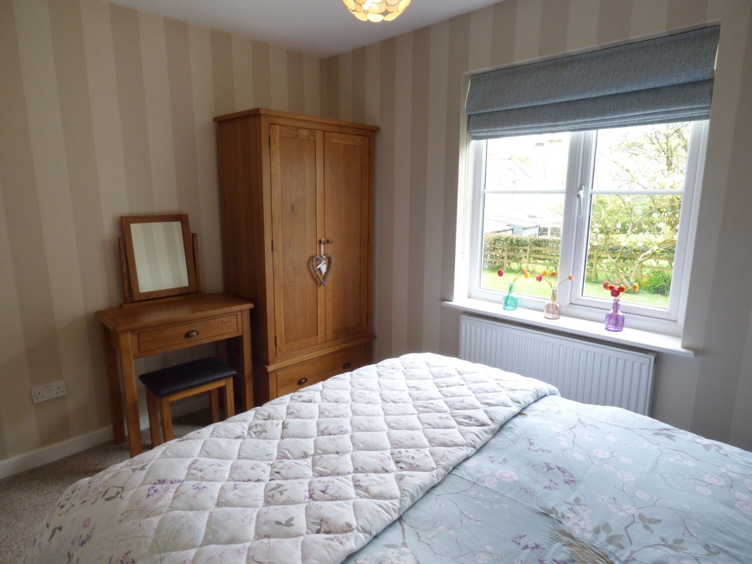 Ein Schlafzimmer mit Bett, einem Holzschrank, einem Schreibtisch mit Stuhl und einem Fenster mit Gartenblick.