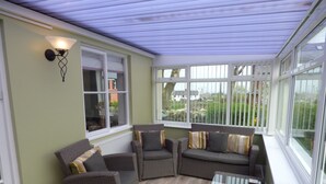Ein Wintergarten mit Korbmöbeln, einem Glastisch und großen Fenstern mit Blick ins Freie.
