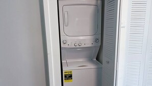Ett kompakt, vitt tvättrum med en tvättmaskin och en torktumlare med frontmatning, en tydlig energimärkning och en dörr med lamellpaneler.