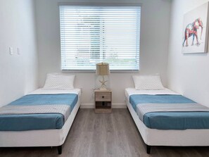 Et værelse med to senge, et natbord, en lampe og et vindue med persienner.