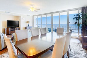 Relax in this spacious living area with a large dining table and comfortable seating for six, featuring a flat-screen TV and sliding glass door to a balcony with ocean views.