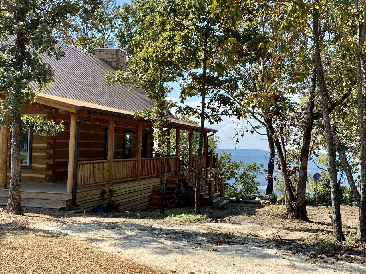 A wooden cabin with a porch, situated in a wooded area with a view of the water.