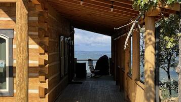 Una cabaña de madera con un porche cubierto que da a una terraza con vistas a un cuerpo de agua.