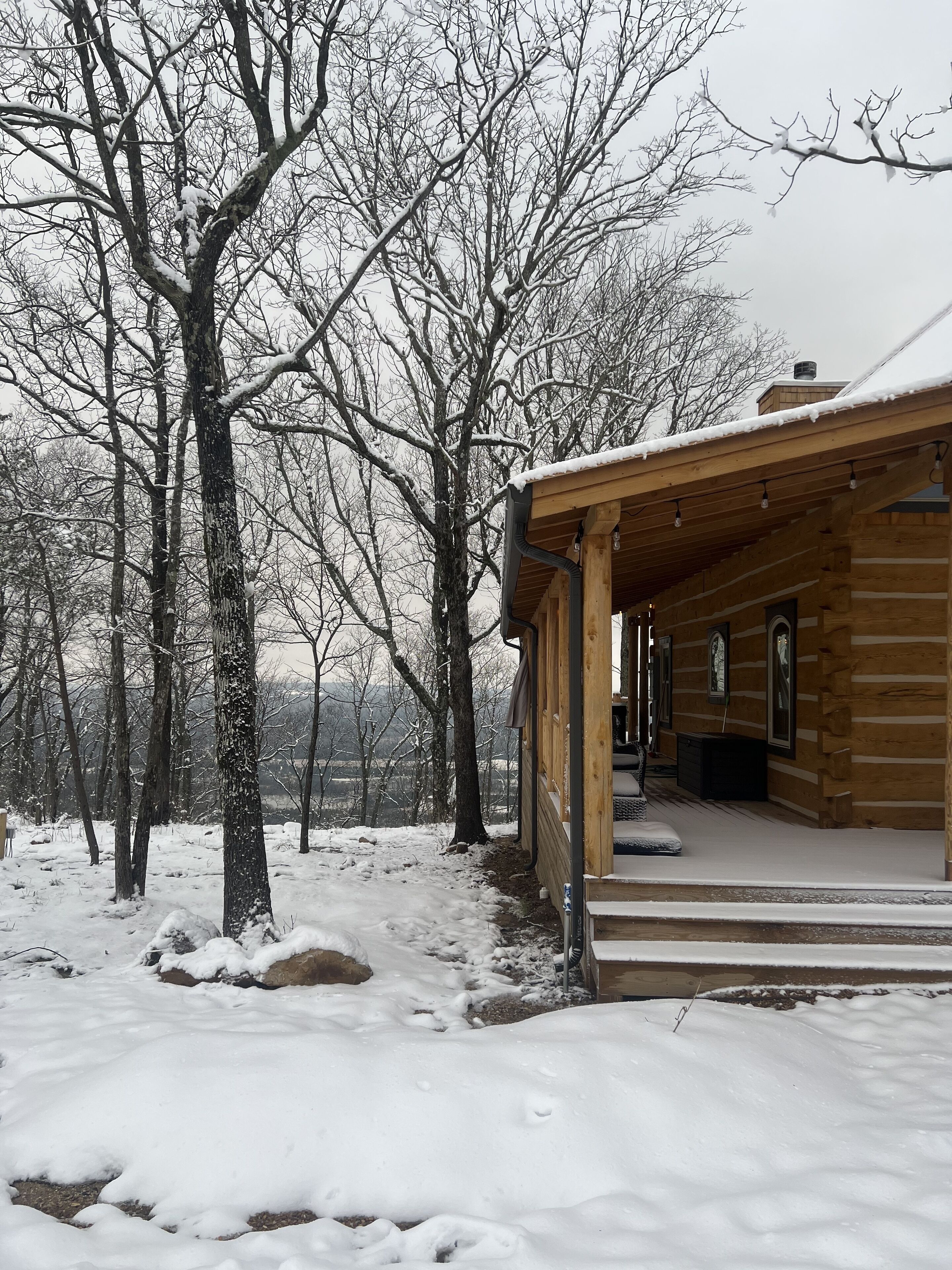 A wooden cabin with a porch, surrounded by snow-covered trees.