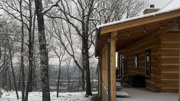 A wooden cabin with a porch, surrounded by snow-covered trees.
