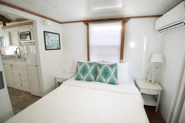 Quarto com uma cama, duas mesas de cabeceira, um abajur branco e uma janela com persianas.