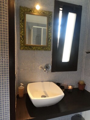 Une salle de bain avec un lavabo blanc, un miroir doté d’un cadre orné et un mur recouvert de carreaux.