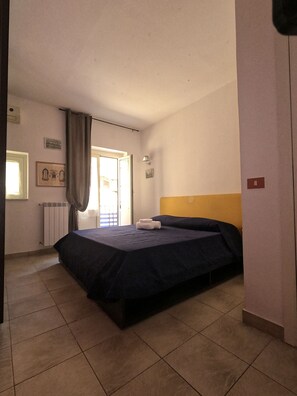 Une chambre à coucher comprenant un lit, un radiateur, une fenêtre avec des rideaux et un luminaire fixé au mur.