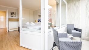 Een moderne hotelkamer met een bed, een zithoek met een tafel en stoelen, en een groot raam met uitzicht op de buitenkant van het gebouw.